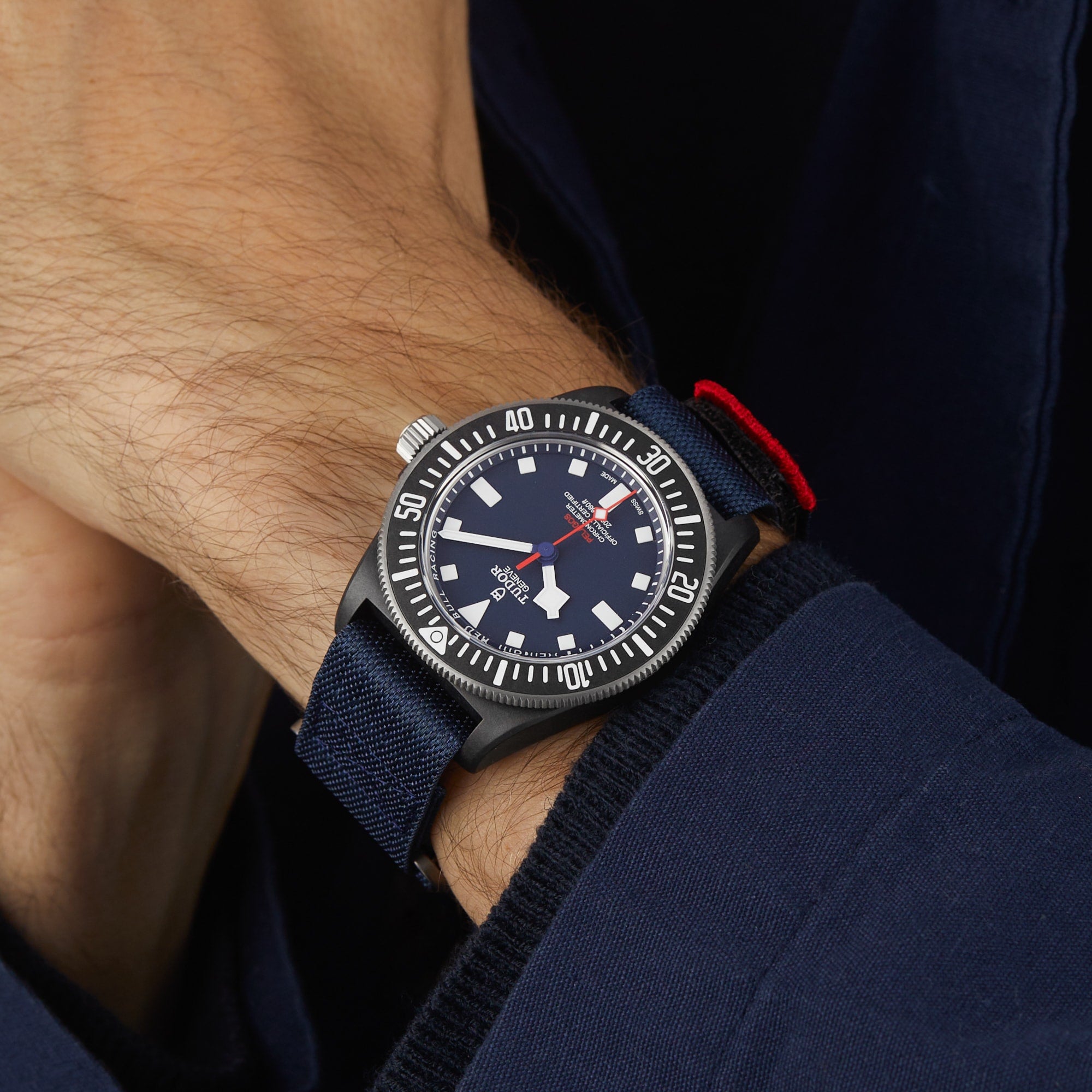 A person wearing a TUDOR Pelagos FXD diver-style watch with a navy blue case, black bezel, white markers, and a waterproof navy blue fabric strap.
