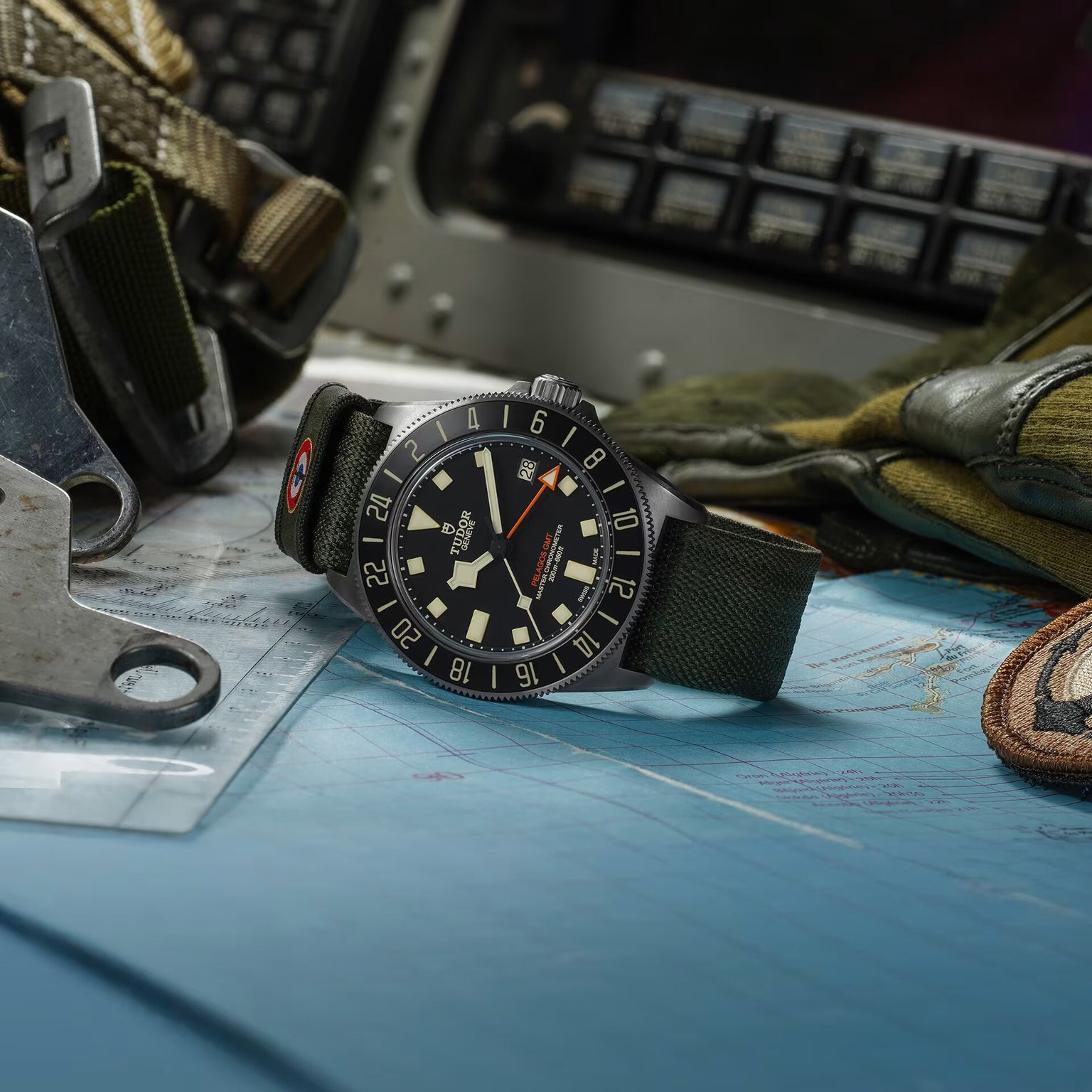 The TUDOR Pelagos FXD GMT, featuring a green strap, is displayed on a map surrounded by flight gear and cockpit controls.