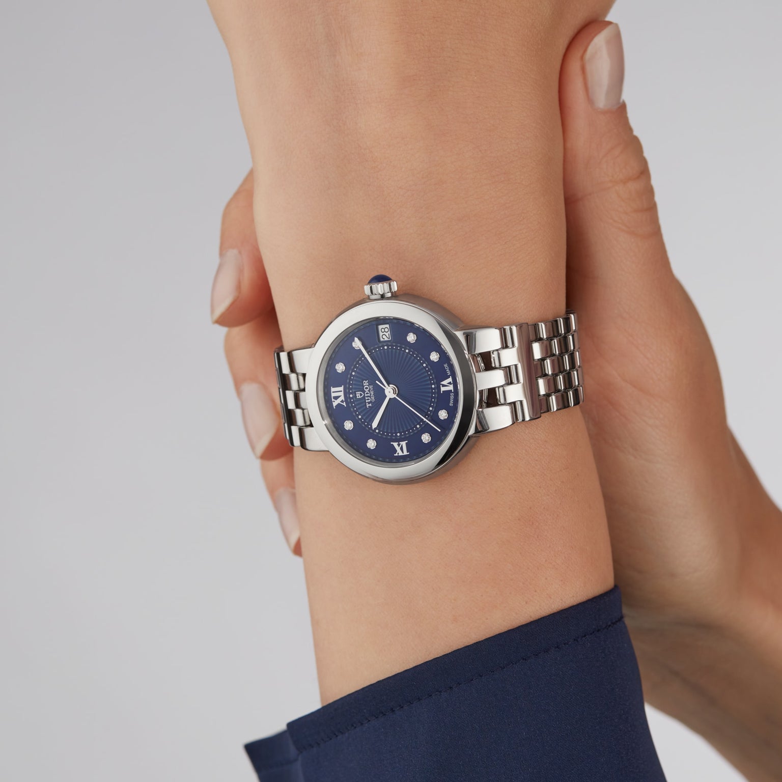 A TUDOR Clair de Rose wristwatch with a silver band and blue face featuring Roman numerals on a persons wrist.