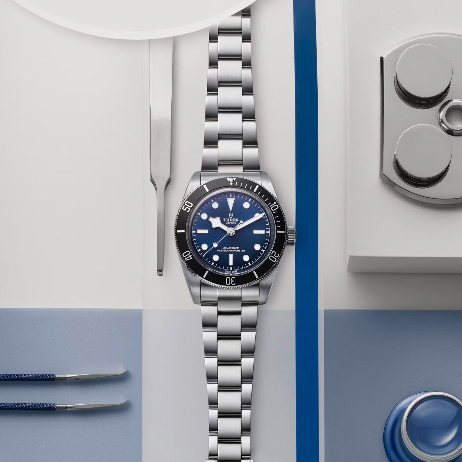A TUDOR Black Bay 68 wristwatch with a blue dial, crafted in stainless steel, displayed amid watchmaking tools on a flat surface.