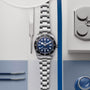 A TUDOR Black Bay 68 wristwatch with a blue dial, crafted in stainless steel, displayed amid watchmaking tools on a flat surface.