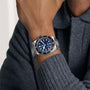 A person wearing a TUDOR Black Bay 68 wristwatch with a blue dial and a grey sweater.