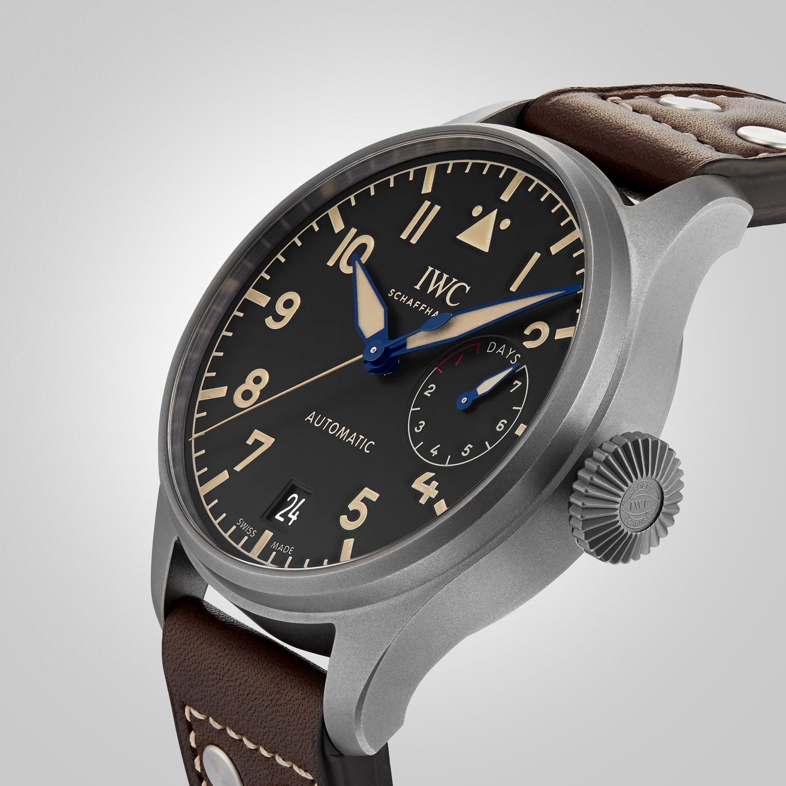 A close-up of the IWC Schaffhausen Big Pilots Watch Heritage, featuring a black dial with beige numerals, day subdial, automatic movement, and a brown leather strap with metal rivets.