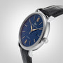 The IWC Schaffhausen Portofino Automatic is a silver wristwatch with a blue dial, gold hour markers, a date window at 3 o’clock, and a black leather strap—an elegant display of Swiss precision.