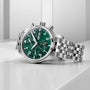 The IWC Schaffhausen Pilots Watch Chronograph 41, featuring a racing green dial and metal bracelet, is displayed on a white geometric surface.