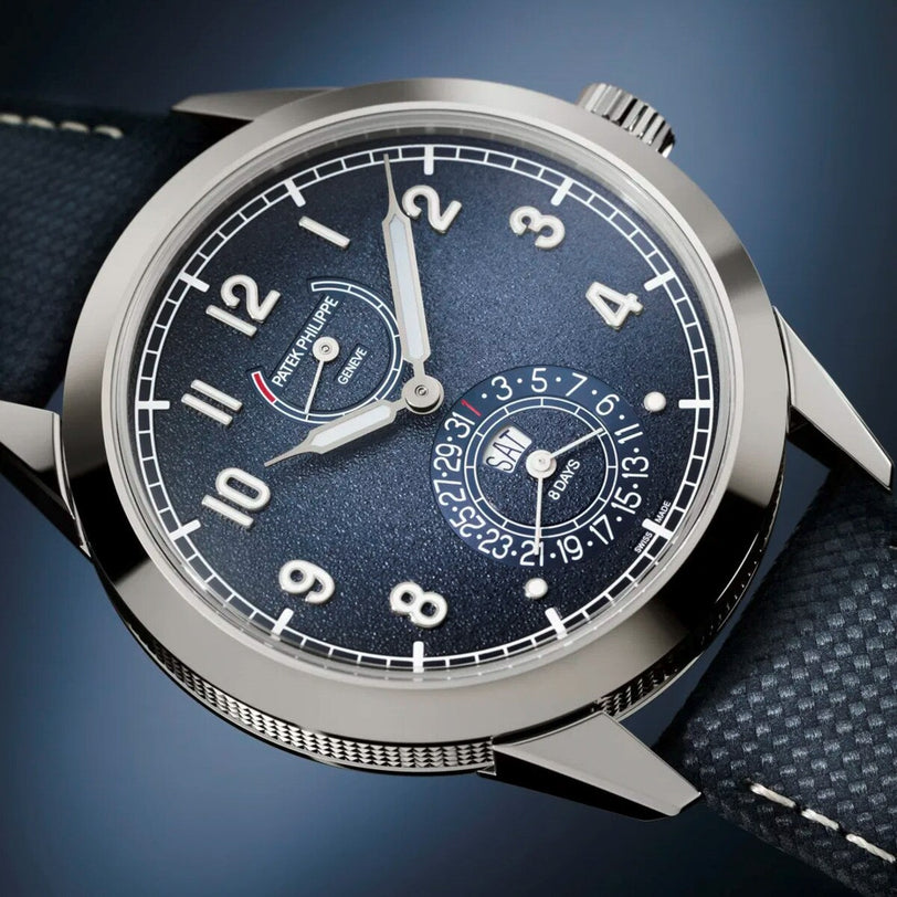 A close-up of the Patek Philippe Complications 5328G-001 luxury blue wristwatch featuring white numerals and a textured strap.