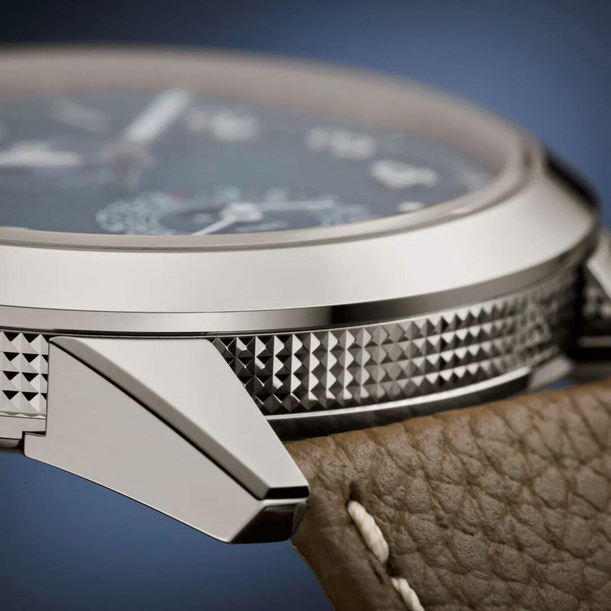 Close-up of the Patek Philippe Complications 5328G-001 watch case, featuring textured metal sides and a brown leather strap with white stitching.