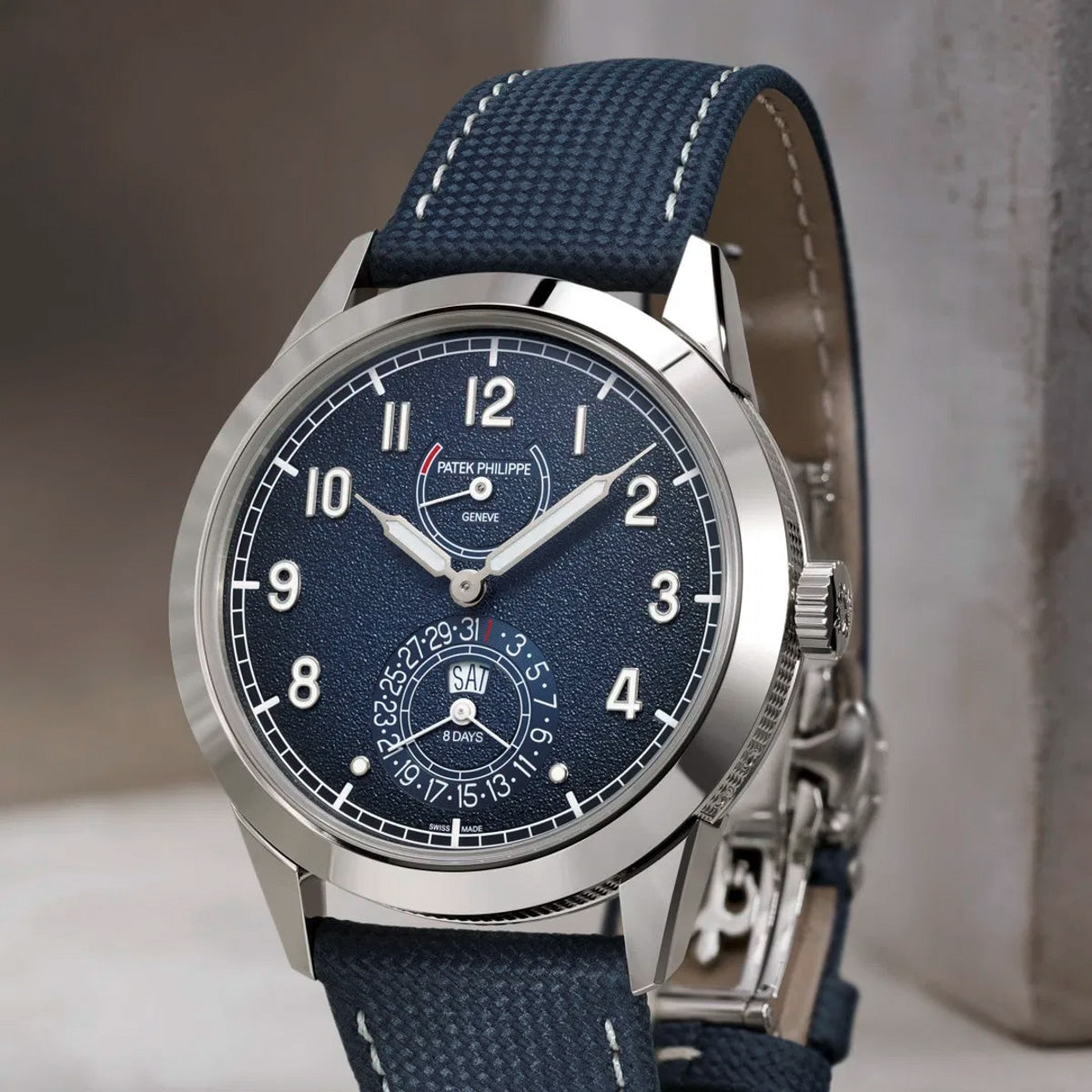 The Patek Philippe Complications 5328G-001 wristwatch features a blue textured dial and matching blue leather strap, displayed upright.