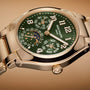 The Patek Philippe Twenty~4 7340/1R-010 is a gold wristwatch featuring a green dial, moon phase, calendar functions, and bold white numerals on a gold band.