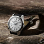 A Grand Seiko Spring Drive Heritage wristwatch with a silver dial and black leather strap rests on a wooden surface.