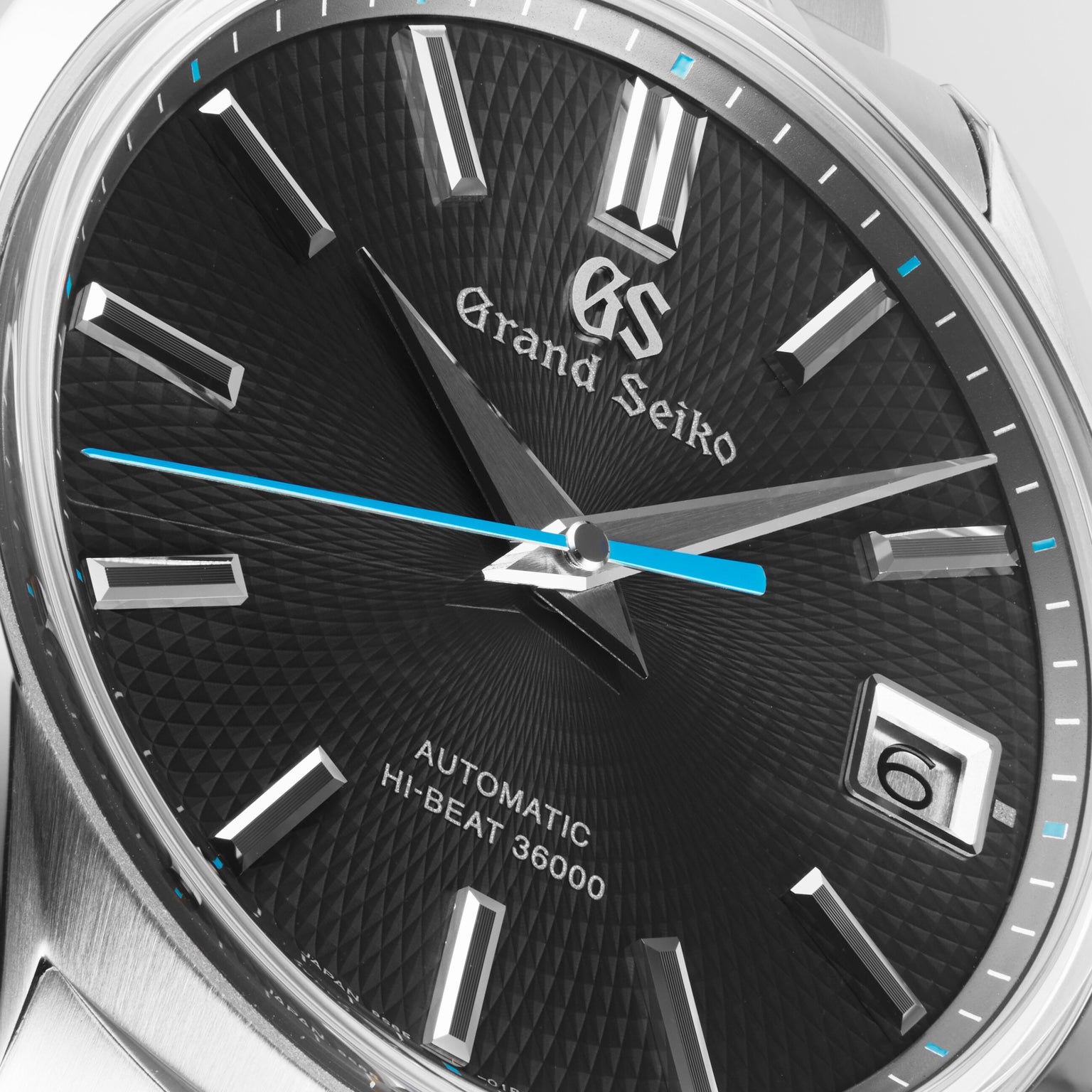 Close-up of the Grand Seiko Hi-Beat Heritage wristwatch, featuring a textured black dial, silver hour markers, blue second hand, and date display at 3 o’clock, inspired by the serene beauty of Jodogahama beach.