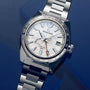 The Grand Seiko Spring Drive GMT Sport features a textured white dial, silver markers, GMT hand, date at 3 o’clock, and a high-intensity titanium bracelet—shown against a blue background.