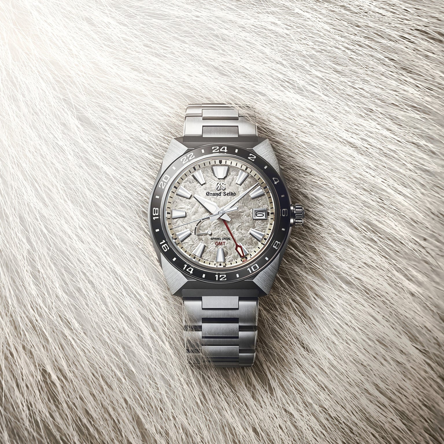The Grand Seiko Spring Drive GMT Sport features a textured dial and GMT bezel, powered by the Spring Drive 9R66 Caliber, shown on a soft, fur-like background.