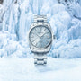 The Grand Seiko Hi-Beat Heritage wristwatch with a frosted light blue dial stands upright amid icy snow formations, highlighting the elegance and resilience of this mechanical timepiece.