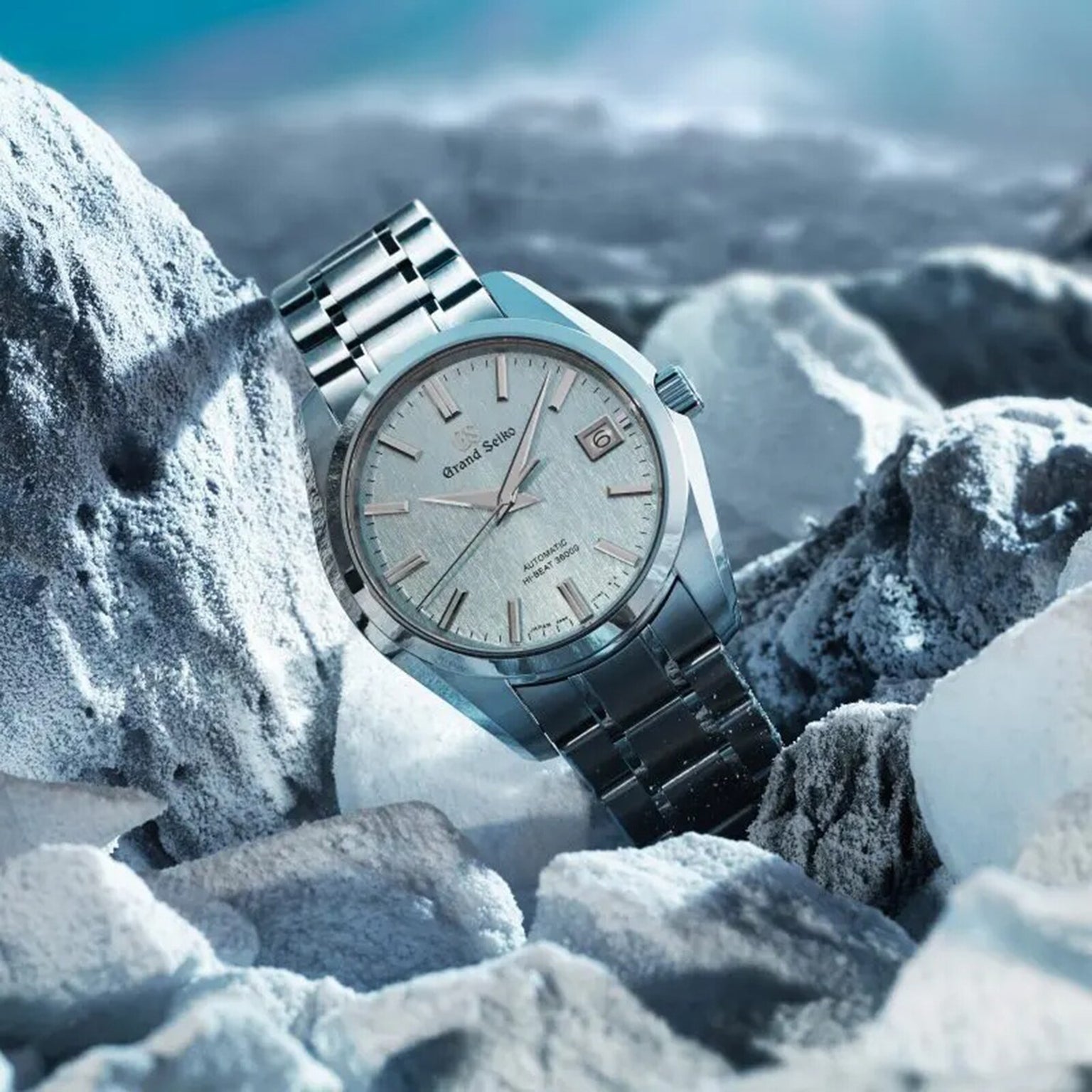 The Grand Seiko Hi-Beat Heritage wristwatch, crafted from High-Intensity Titanium with a textured white dial, is displayed among ice-like rocks beneath a blue sky.