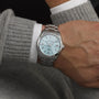 Someone wears a Grand Seiko Hi-Beat Heritage watch with a light blue textured dial, paired with a long-sleeved grey sweater and a visible white shirt cuff.