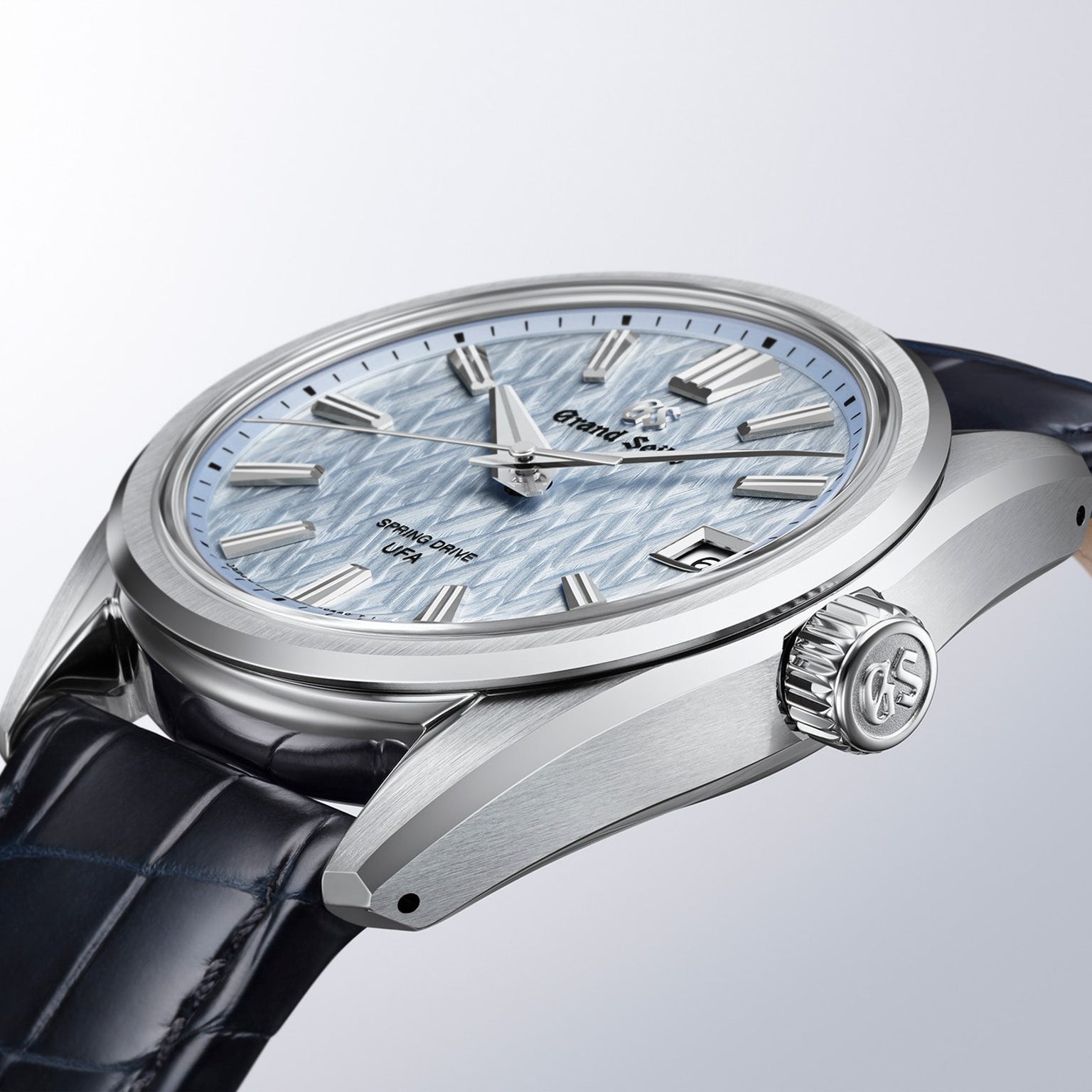 The Grand Seiko Spring Drive U.F.A Evolution 9 is a silver wristwatch featuring a textured light blue dial and a dark leather strap.