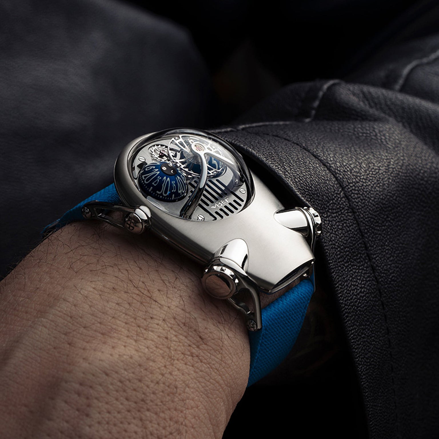 A futuristic MB&F Horological Machine N°10 Bulldog wristwatch in silver with blue accents is worn over a dark sleeve.