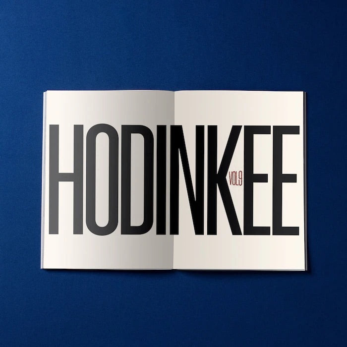 An open HODINKEE Magazine, Volume 9 by Hodinkee shows HODINKEE in bold black and VOL 9 in small red on a white page against a dark blue background—ideal for watch enthusiasts.