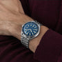 A person wearing the DOXA Sub 200 Caribbean, a 316L stainless steel divers watch with a blue dial and silver hour markers, dressed in a burgundy long-sleeve garment.