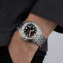 A person wearing a DOXA Sub 300T Sharkhunter—silver analog divers watch with a black dial, white Super-LumiNova markers, and an orange minute hand—paired with a dark long-sleeve shirt.