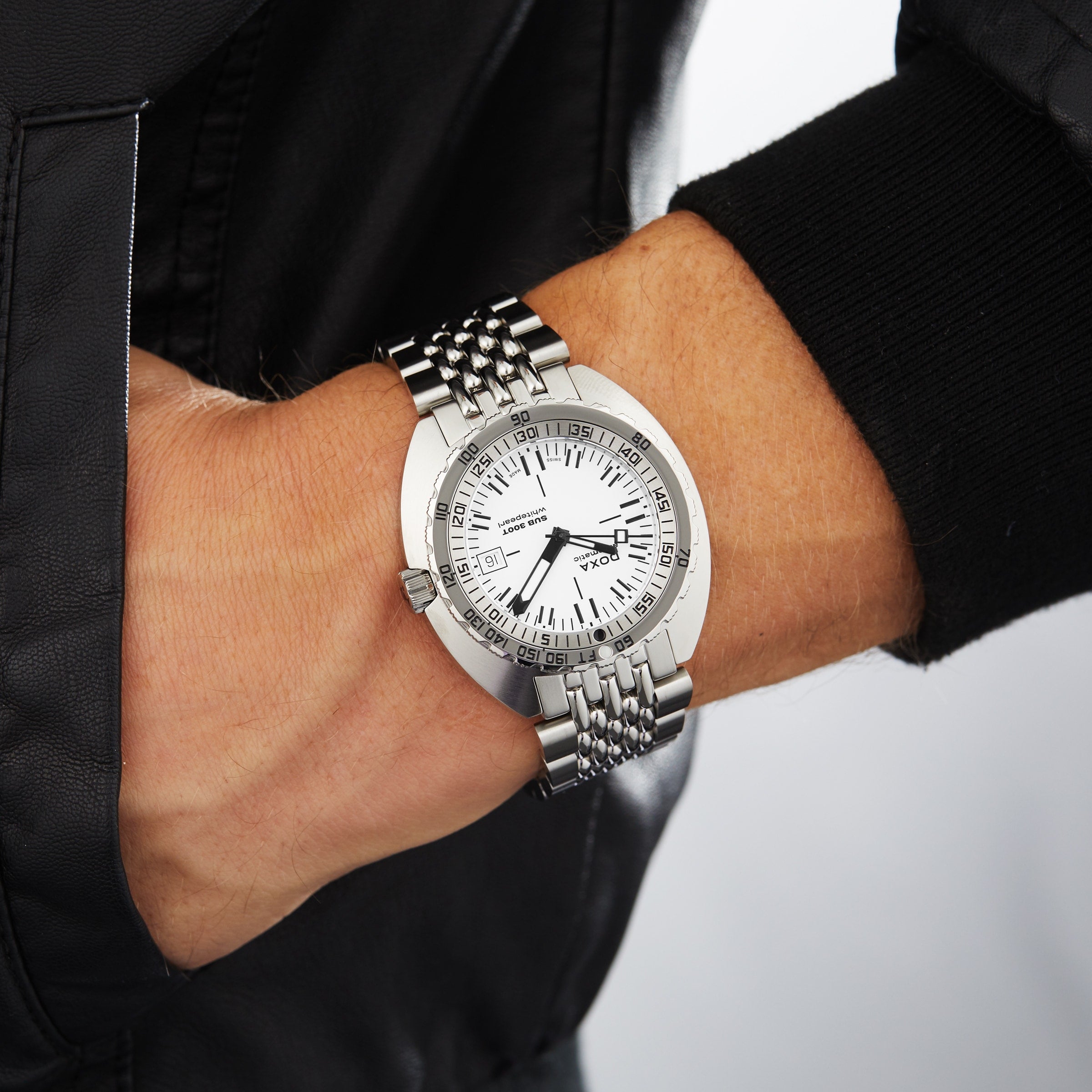 Someone wearing the DOXA Sub 300T Whitepearl, a silver wristwatch with a white dial and metal band, has their hand in their jacket pocket.
