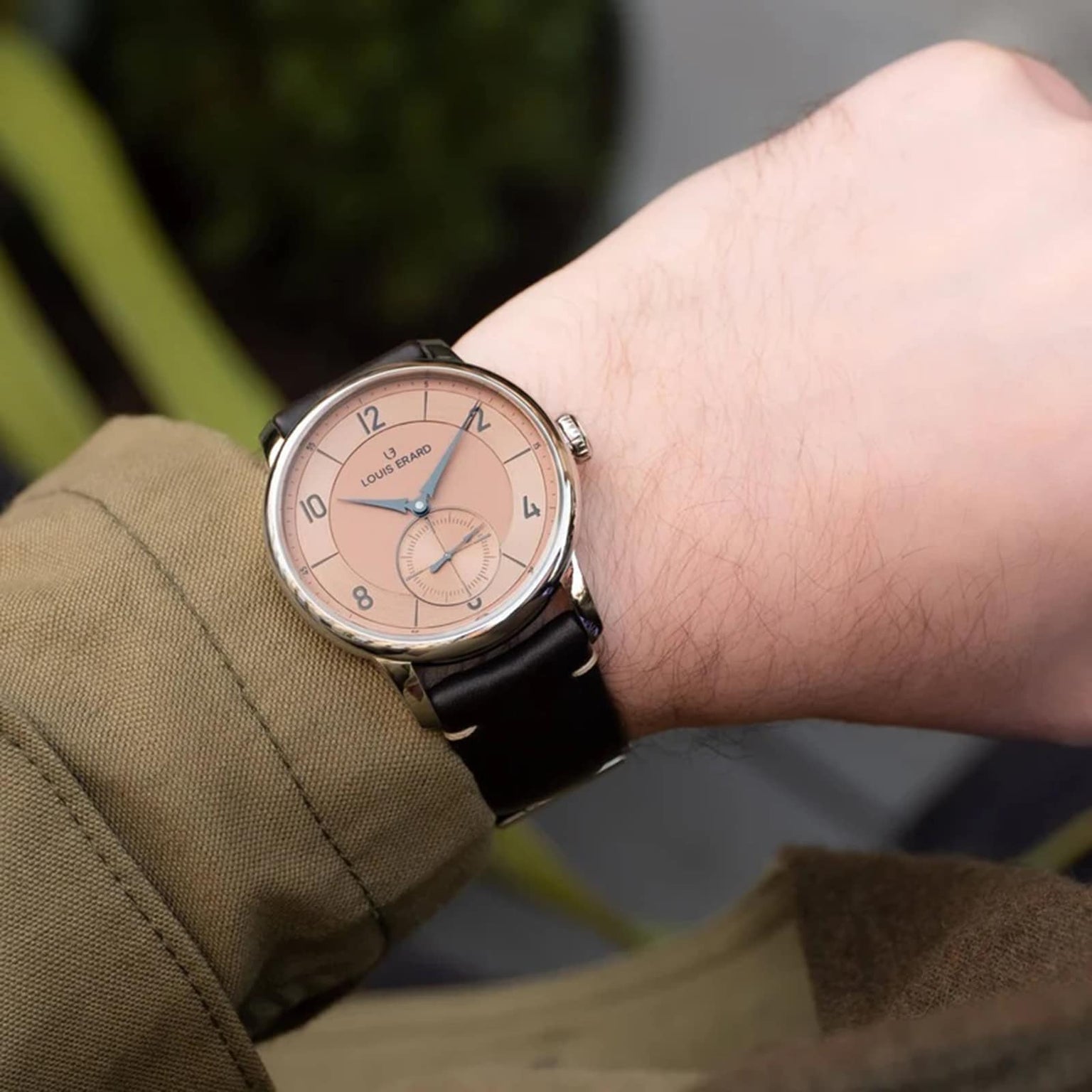 A person wearing a Louis Erard Petite Seconde Terracotta 42 wristwatch with a tan dial and black leather strap, seen from above.