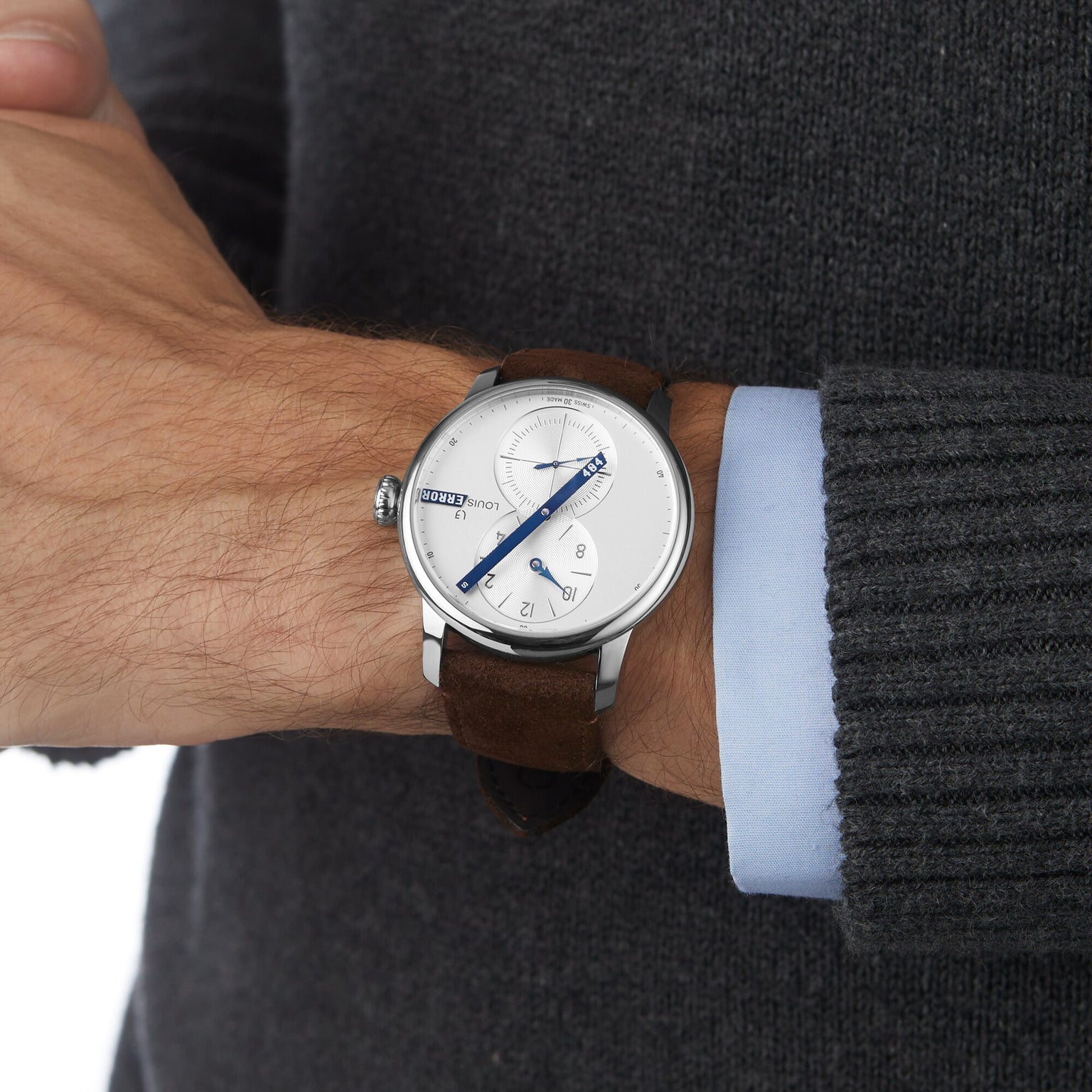 A person wearing the Louis Erard Le Régulateur Louis Erard x seconde/seconde/, a silver wristwatch with a white face and brown leather strap, over a gray sweater.