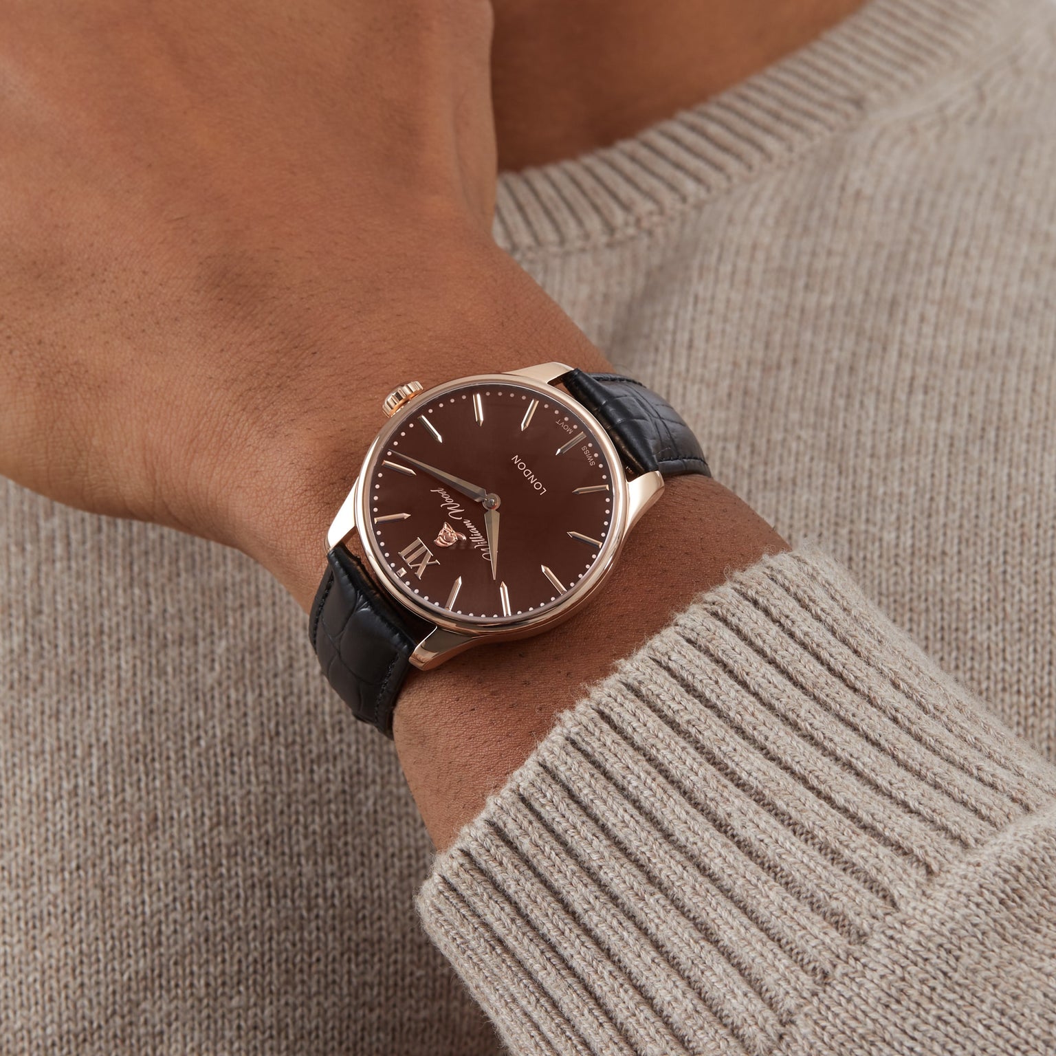 A person wearing the William Wood Chivalrous Collection - Chocolate watch with a black leather strap and a beige knit sweater.
