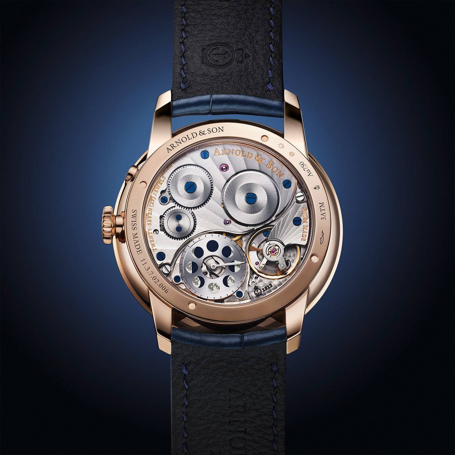 Close-up of Arnold & Son Perpetual Moon 41.5mm Red Gold’s intricate exposed movement, gold casing, and black leather strap.