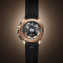 The Angelus Chronodate Gold Black features a gold casing, black leather strap, and exposed mechanical back, displayed against a brown background.