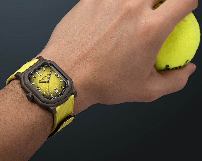 A hand wearing the Gerald Charles Maestro GC Sport Tennis Limited Edition yellow watch holds a yellow tennis ball against a dark background.