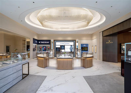 Luxury watch store with glass display cases, bright lighting, and brand signs for Rolex, TAG Heuer, and Ulysse Nardin.