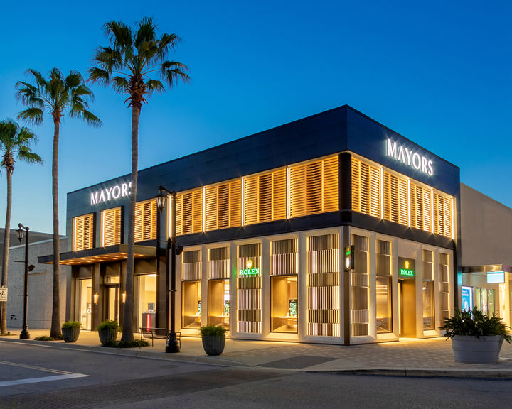Modern Mayors jewelry store with illuminated signs and palm trees at dusk.