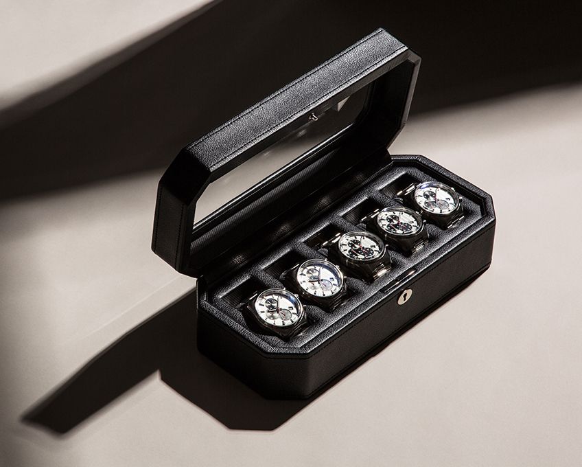 Black leather watch box with handle holds five watches with white dials in individual cushioned slots.
