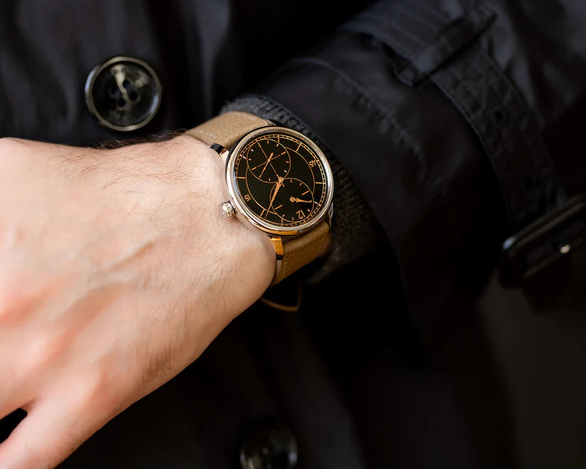 Close-up of a person wearing a watch with a dark face and brown leather strap, against a dark background.