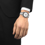 Hand wearing a silver watch with a black and white face, against a plain background