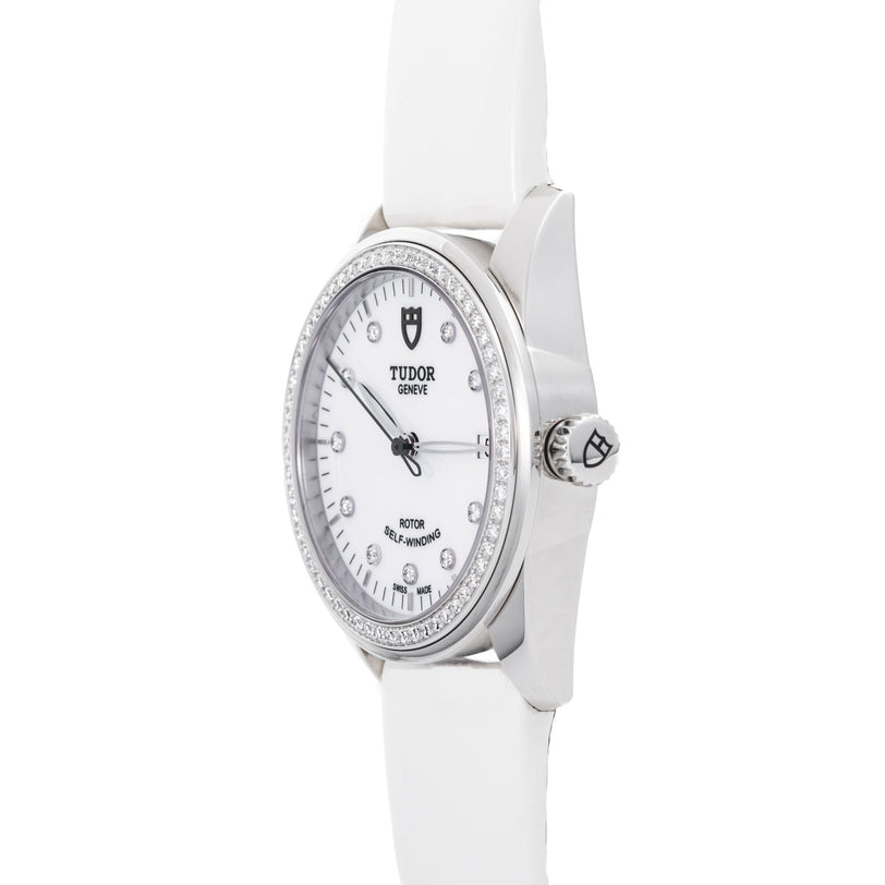 The TUDOR Glamour Date wristwatch features a white dial with diamond hour markers and a white leather strap, shown from an angled perspective.