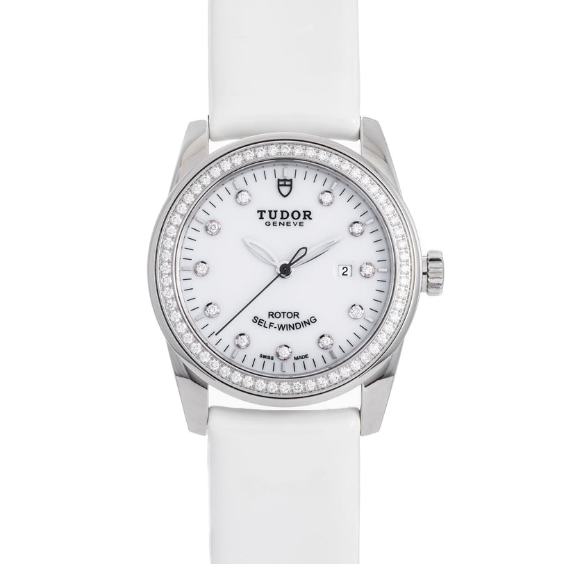 The TUDOR Glamour Date wristwatch features a white face, diamond hour markers, and a white strap.