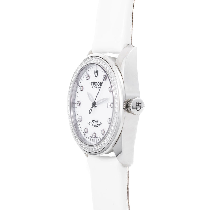 The TUDOR Glamour Date wristwatch features diamond hour markers, a silver bezel, and a white leather strap, viewed from an angle.