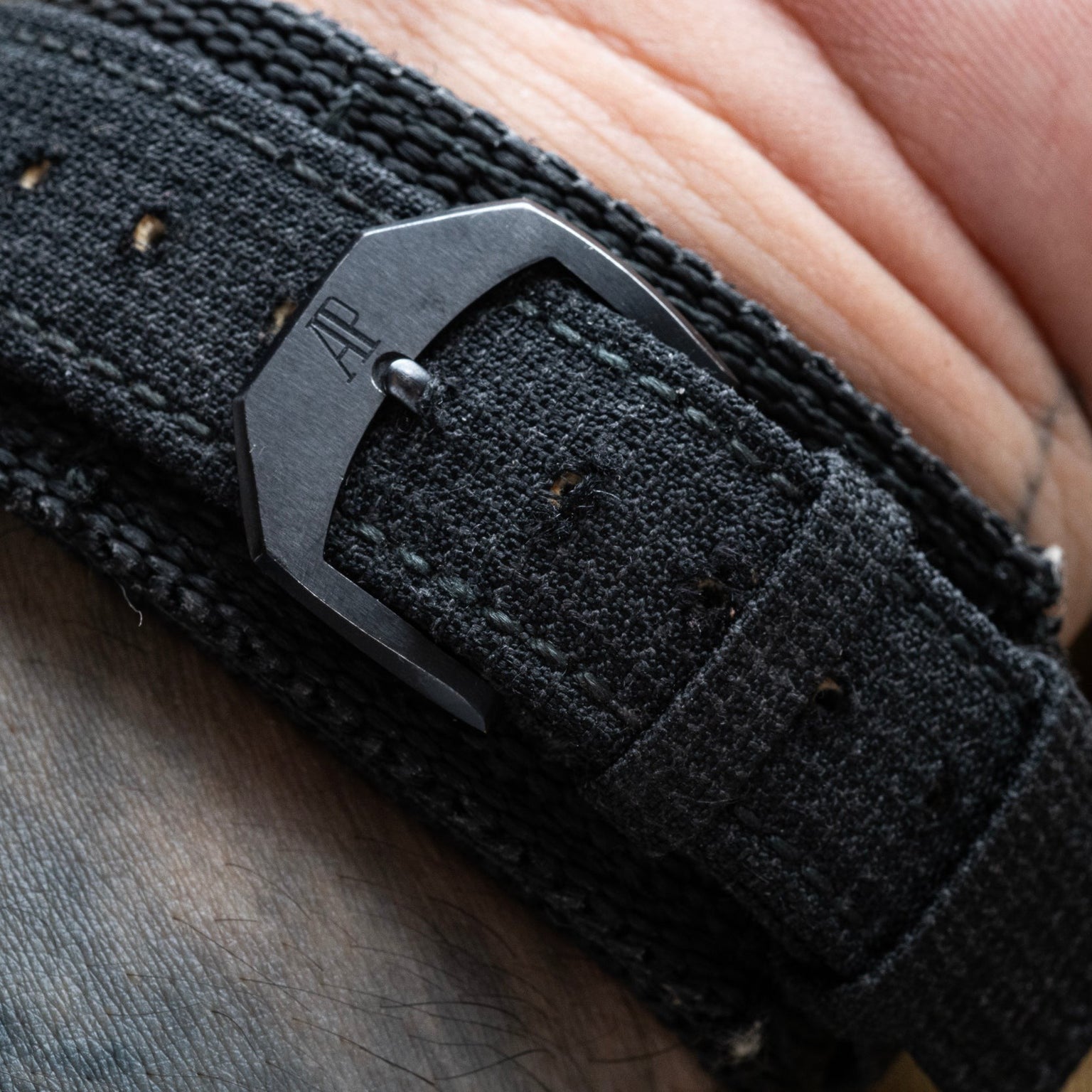 Close-up of a fabric strap with a black buckle engraved AP on a wrist, from the Audemars Piguet Royal Oak Offshore End of Days.
