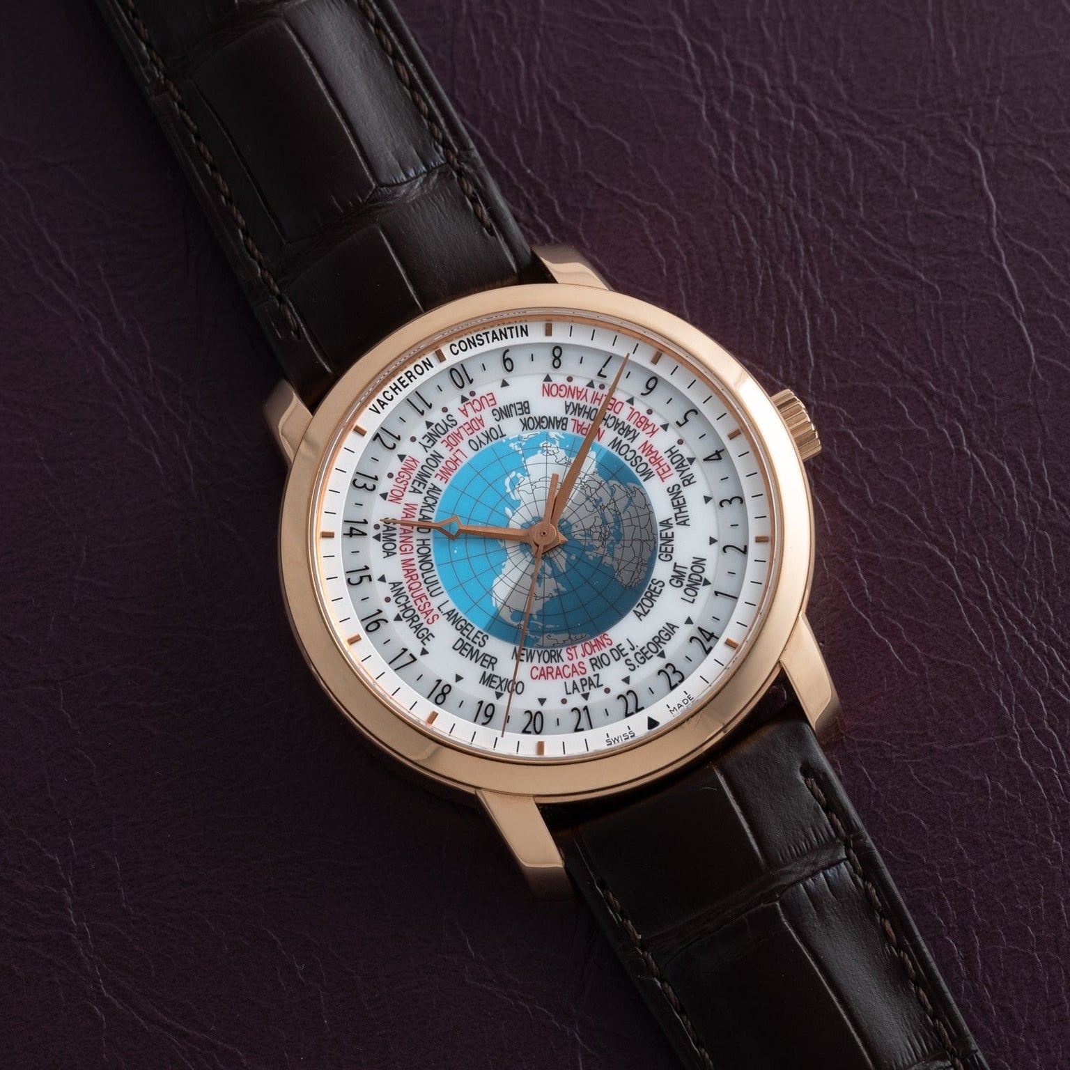 The Vacheron Constantin Traditionnelle World Time, featuring a brown leather strap, is showcased on a textured dark purple surface.