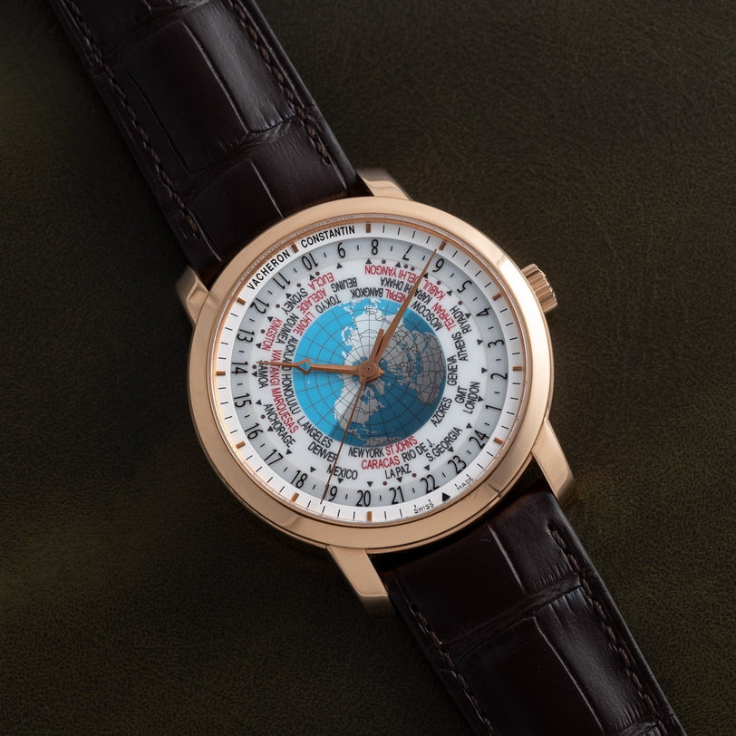 The Vacheron Constantin Traditionnelle World Time is a luxury wristwatch featuring a world map dial, city names, and a brown leather strap displayed on a dark surface.