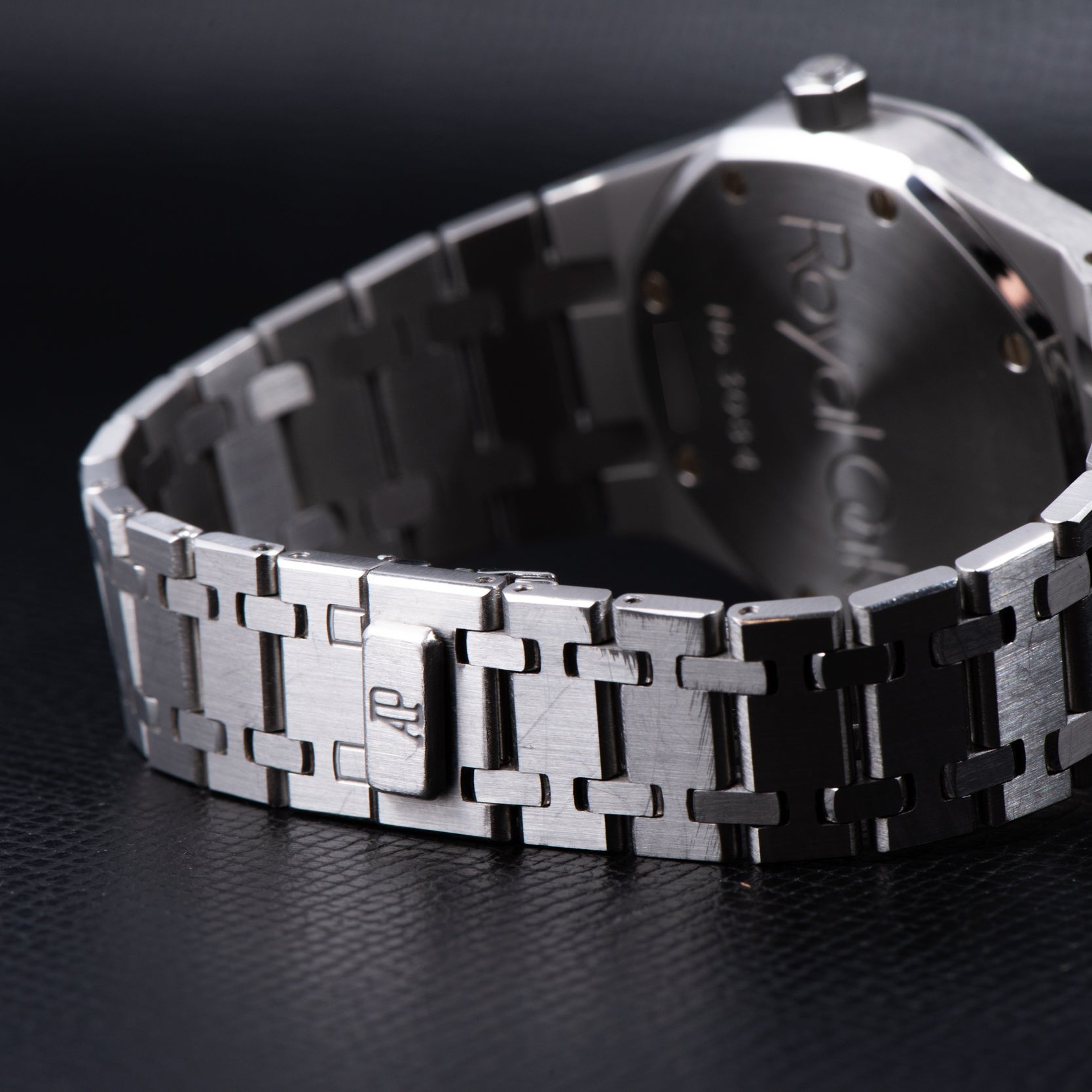 Close-up of the Audemars Piguet Royal Oak Day-Date Moonphase’s silver metal bracelet, featuring the AP logo on the clasp, resting on a black surface.