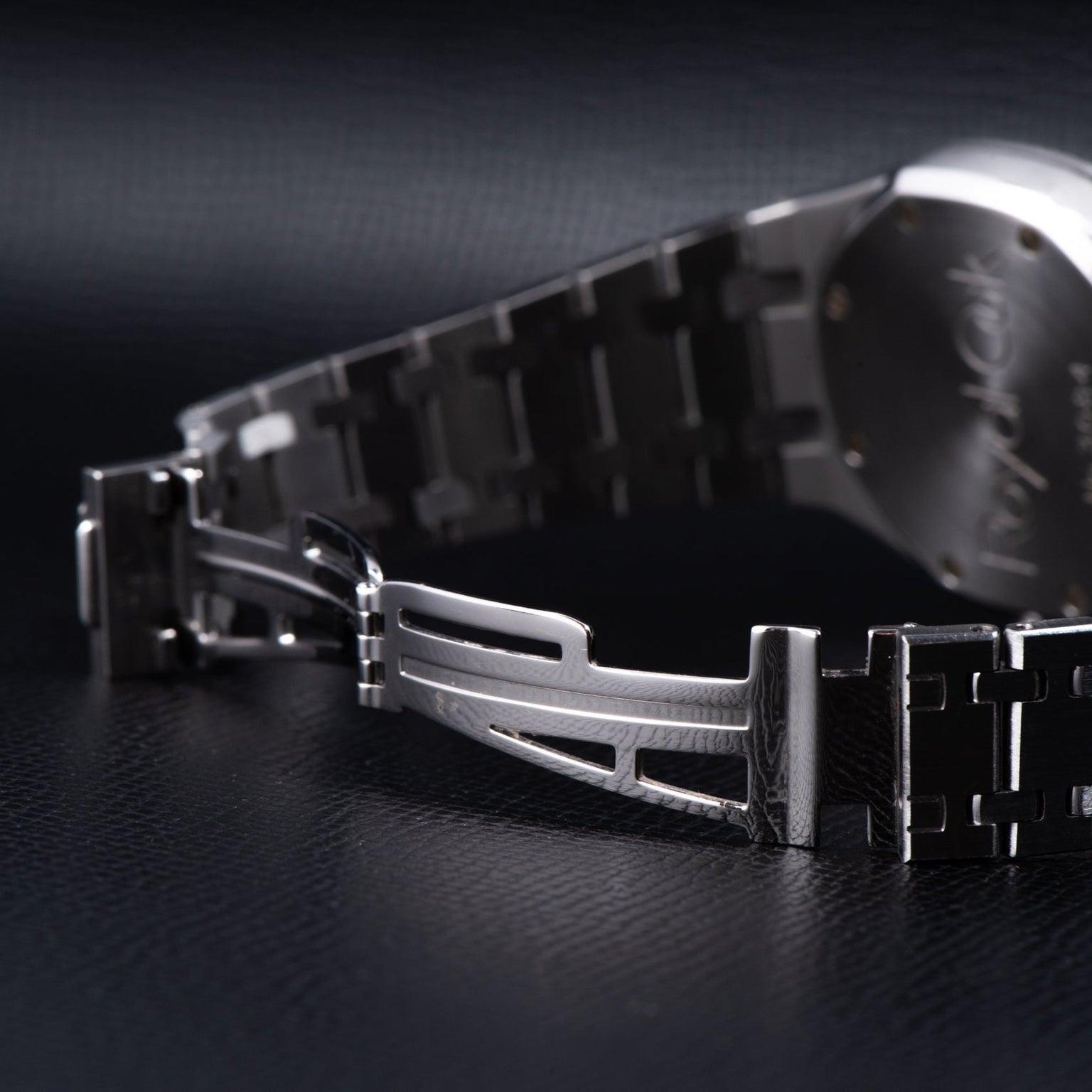 Close-up of the Audemars Piguet Royal Oak Day-Date Moonphase watch’s metal clasp and bracelet resting on a dark, textured surface.
