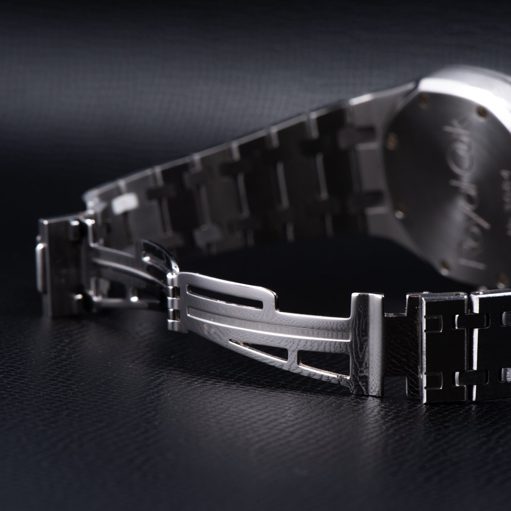Close-up of the Audemars Piguet Royal Oak Day-Date Moonphase watch’s metal clasp and bracelet resting on a dark, textured surface.