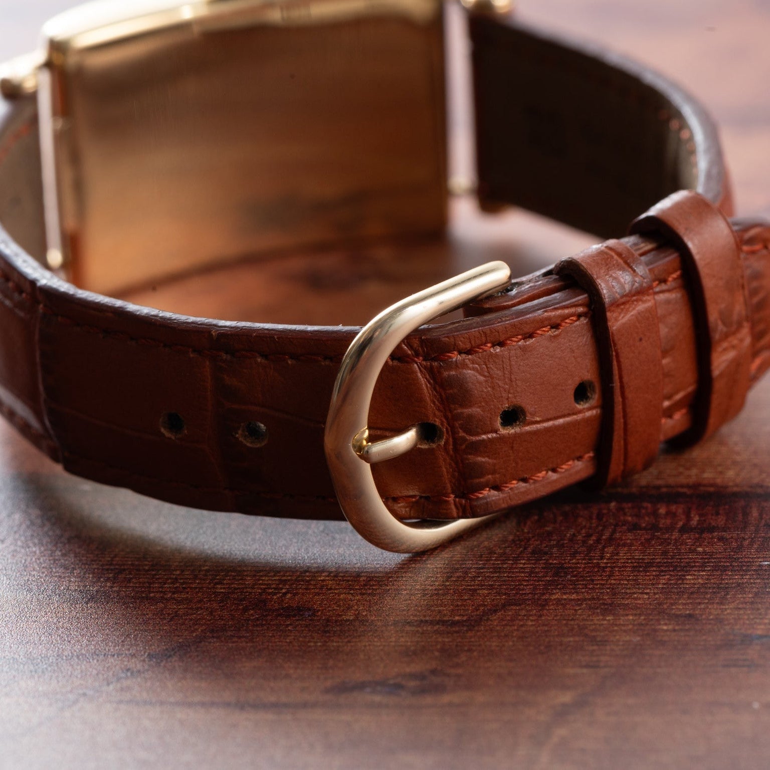 Close-up of the Patek Philippe Birks Rectangular Dress Watch’s brown leather strap with a gold buckle, displayed on a wooden surface.