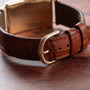 Close-up of the Patek Philippe Birks Rectangular Dress Watch’s brown leather strap with a gold buckle, displayed on a wooden surface.