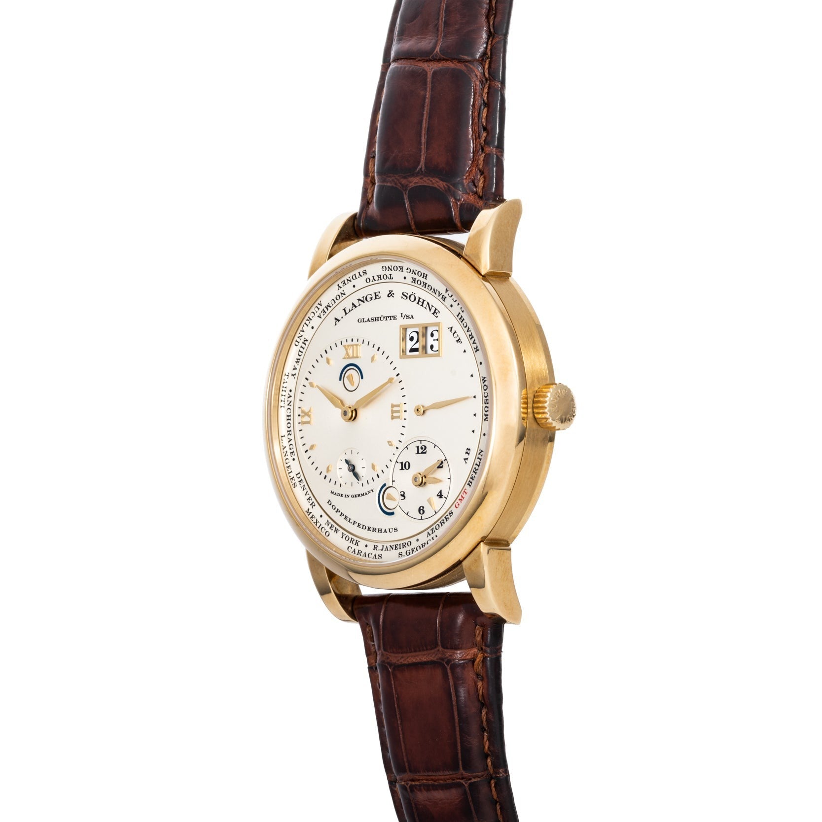 The Lange & Sohne Lange 1 Timezone features multiple dials, a gold case, brown leather strap, and a white face with black text and numbers.