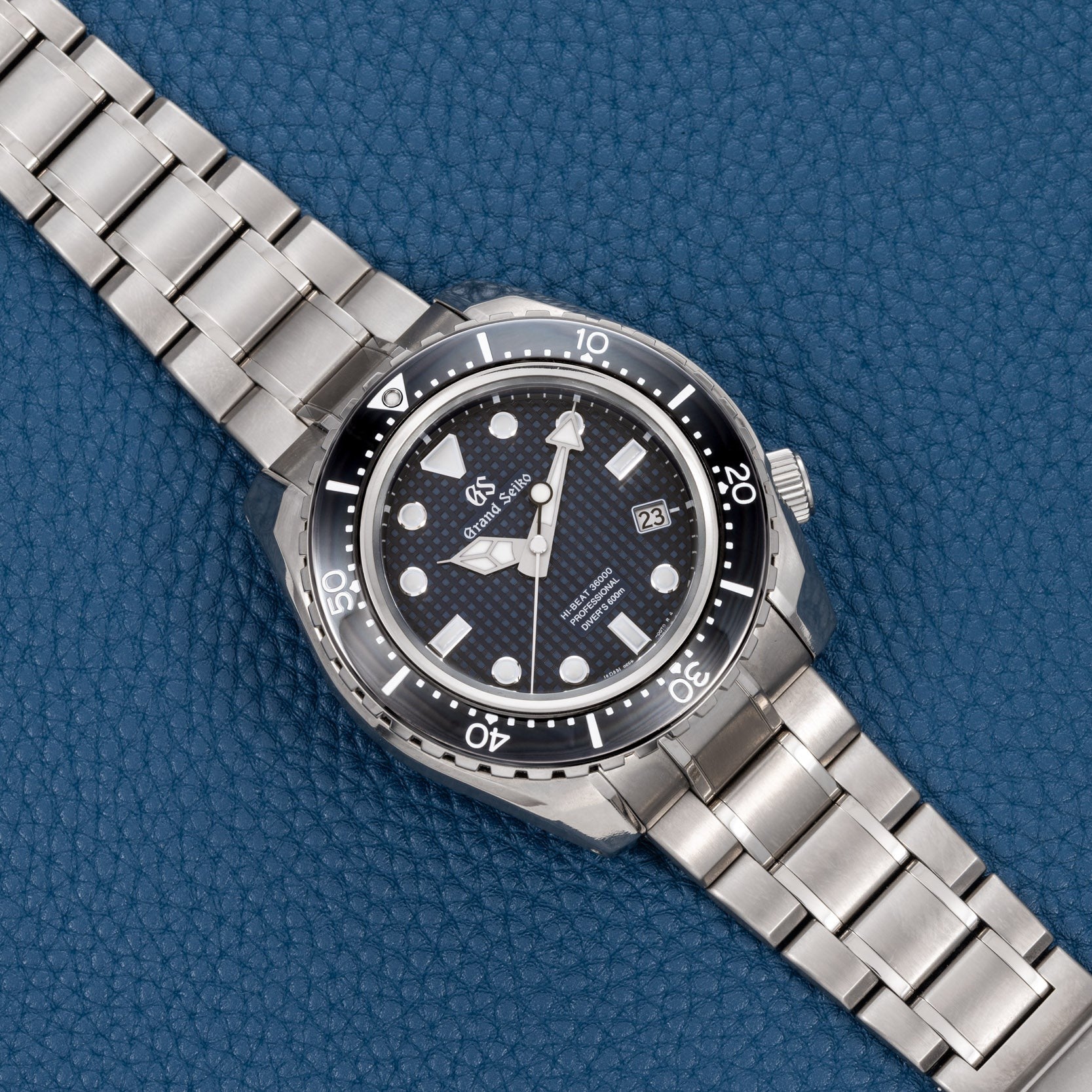 A Grand Seiko Hi-Beat Professional 600m Divers Limited Edition silver watch with a black bezel rests on a blue textured surface.